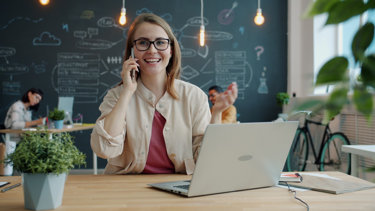 Donna con occhiali parla al telefono in un ufficio moderno.