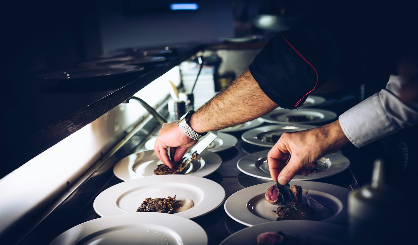 Chef impiattare meticolosamente piatti gourmet in una cucina professionale.